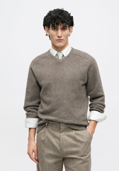 Maglione a maglia marrone con scollo a V, caratterizzato da una texture morbida. Abbinato a pantaloni a quadri su misura e una camicia bianca sotto.