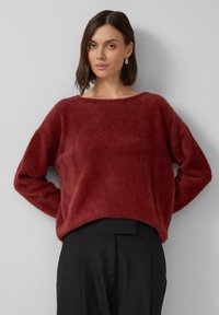 Maglione morbido bordeaux con scollatura a barca e spalle scese, abbinato a pantaloni neri. Texture soffice, vestibilità comoda e design di lunghezza media.