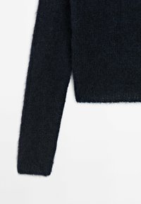 Manche de pull noir en maille duveteuse et ourlet court sur fond blanc, montrant la texture et le détail du tissu.