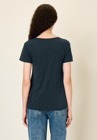 Temno modra kratka majica s kratkimi rokavi in okroglo ovratnikom, z gladko teksturo, v kombinaciji s svetlo modrimi jeans hlačami, ki imajo zadnje žepke.