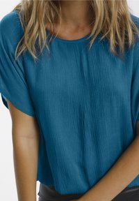 Top blu corto a maniche corte con un tessuto texturizzato e una vestibilità ampia. Dotato di scollatura rotonda e sottili righe verticali. Morbido sulla pelle.