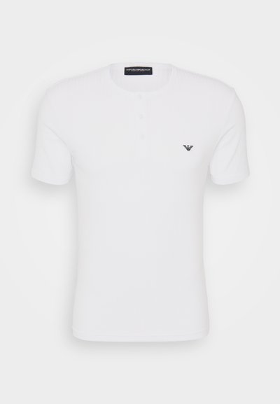 T-shirt branca de manga curta com textura em canelado, decote redondo e faixa de três botões. Apresenta um pequeno logótipo preto no lado esquerdo do peito.