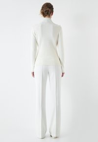 Suéter blanco de cuello alto con una tela texturizada, que presenta una silueta ajustada. Combinado con pantalones acampanados blancos y calzado a juego.