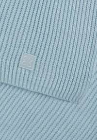 Tissu tricoté bleu clair avec une texture côtelée, comportant une étiquette carrée avec un motif floral dans le coin. Apparence douce et légère.