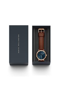 Orologio con cinturino in pelle marrone, cassa in oro rosa, quadrante blu e dettagli dorati, esposto in una scatola blu scuro con un rivestimento interno morbido.