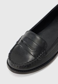 Mocassins en cuir noir avec un design cousu et une bride horizontale sur le cou-de-pied. Texture lisse et bout arrondi. Semelle profilée basse.