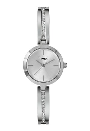 Montre Timex argentée avec un cadran rond, texture métallique brossée, index horaires simples et un bracelet orné d'accents en pierre précieuse transparente.