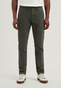 Olijfgroene chinos van een gestructureerde stof, slim fit design, knoopsluiting en zijzakken, gecombineerd met witte sneakers.