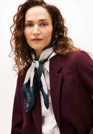 Sciarpa di seta blu navy e panna con motivo astratto, annodata intorno al collo, abbinata a un blazer bordeaux sopra una camicia bianca.