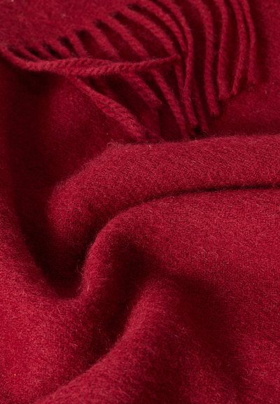 Κόκκινο υφαντό ύφασμα από μαλλί με απαλή υφή, που διαθέτει υφαντό σχέδιο και φουντωτά άκρα, δημιουργώντας απαλές πτυχώσεις και μια ζεστή εμφάνιση.