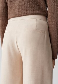 Beige op maat gemaakte broeken met een gladde textuur, voorzien van twee achterzakken. De stof lijkt lichtgewicht en ademend. De tailleband is plat.