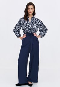 Niebieska bluzka w kwiatowy wzór z bufkami, zestawiona z granatowymi spodniami o wysokim stanie i szerokich nogawkach. Czarn footwear dopełnia stylizację.