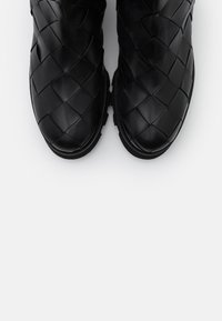 Stivali in pelle intrecciata nera con superficie texturizzata e punta rotonda, dotati di suola flessibile e dettagli di cucitura discreti lungo i bordi.