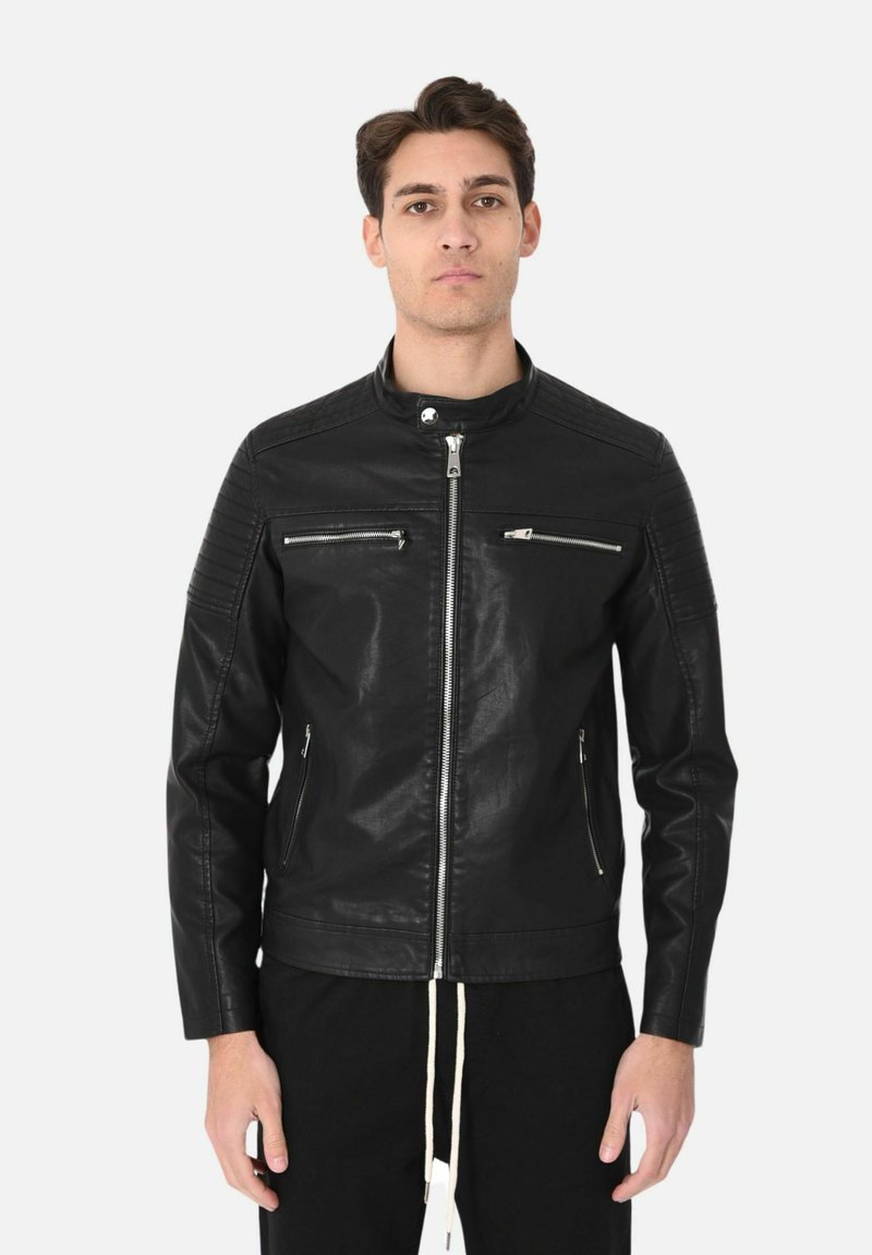 Giacca di pelle nera con colletto alto, apertura con zip e due tasche sul petto. Presenta dettagli a coste su spalle e braccia.