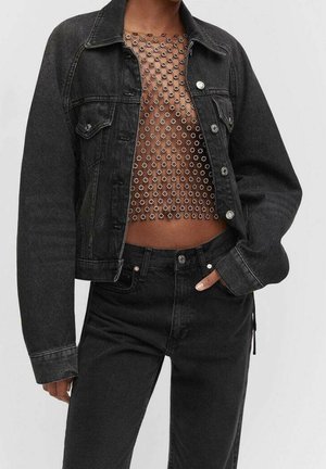 Personne portant une veste en jean noire et un pantalon avec un crop top en résille transparent décoré de clous argentés en forme de fleur.
