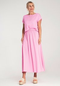 Różowa midi sukienka o luźnym kroju, z elastyczną talią i krótkimi rękawami. Noszona z beżowymi sandałami na platformie. Gładka tekstura, casualowy fason.
