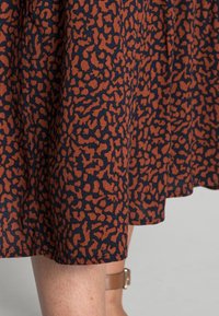 Jupe fluide avec un motif abstrait noir et rouille portée par une personne avec la jambe inférieure nue et une sandale à bride cheville couleur tan.