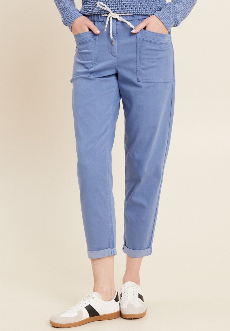 Pantaloni azzurri chiari, a sigaretta, con vita elasticizzata, coulisse, due tasche frontali e orli arrotolati. Abbinati a sneaker bianche.