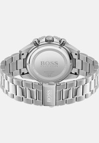 Montre en acier inoxydable argenté avec un bracelet à maillons, un boîtier rond et plusieurs couronnes. Présente un logo sur le fermoir et à l'arrière.