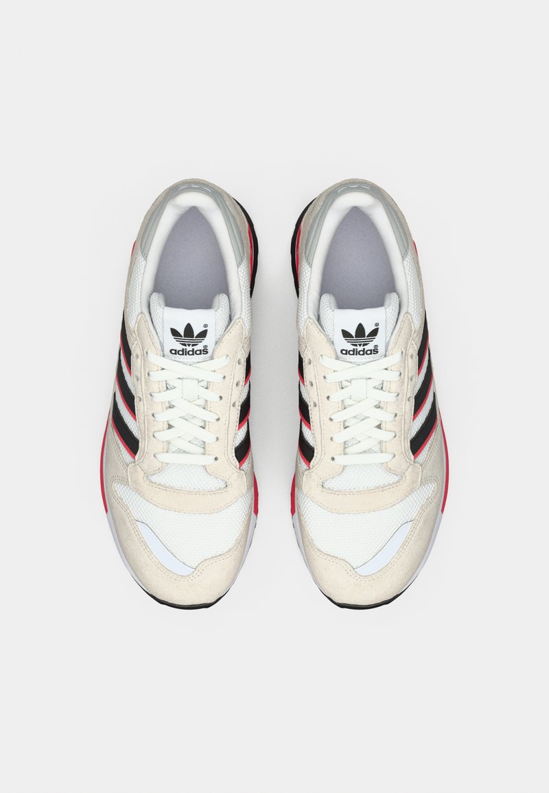 Paar weiße Adidas-Sneakers mit schwarzen und roten Streifen, von oben betrachtet und nebeneinander auf einem schlichten Hintergrund platziert.