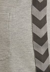 Grauer Sweatshirtstoff mit einer Tasche; mit einem vertikalen schwarzen und grauen Chevron-Musterband an der Seite. Weiche Textur.