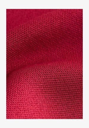 Tekstilstof i dyb rød med en vævet tekstur og små, jævne mønstre, der udviser bløde folder og en glat overflade.