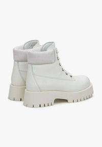 Witte leren enkelboots met een lichtgrijze suède kraag, zes metalen oogjes en een chunky witte rubberen zool met diepe noppen.