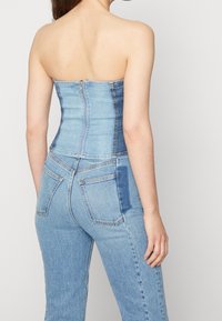 Blå denim langklänning utan axelremmar med figursydd kropp, vertikala sömmar och dragkedjestängning bak. Har tvåtonad denim för texturvariation.