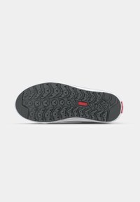 Semelle de chaussure avec motif de bande de roulement texturé noir, détail rectangulaire rouge central, et semelle intermédiaire blanche visible de dessous sur fond gris.