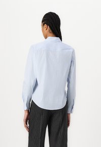 Camicia a righe blu chiaro con colletto a punta, maniche lunghe e orlo curvo. Il tessuto sembra liscio con una texture leggera.
