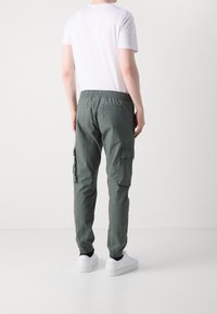 Zielone spodnie typu cargo z elastycznym pasem, bocznymi kieszeniami i zwężanymi nogawkami. Połączone z prostym białym t-shirtem i białymi trampkami.