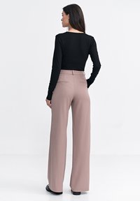 Czarny, długi rękaw top połączony z jasnoróżowymi, wysokimi spodniami o szerokich nogawkach; gładki materiał z tylnymi kieszeniami i dopasowanym krojem, noszony z płaskimi butami.