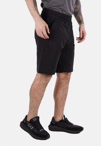 Shorts atletici neri realizzati in morbido tessuto, con vita elasticizzata e cordoncino. Indossati con scarpe da ginnastica nere e una t-shirt grigia.