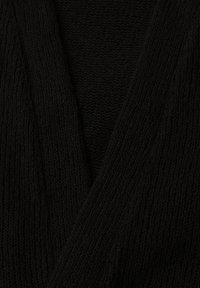 Gros plan sur un tissu tricoté noir avec un motif côtelé en forme de col en V, montrant la texture détaillée et les variations de couture.