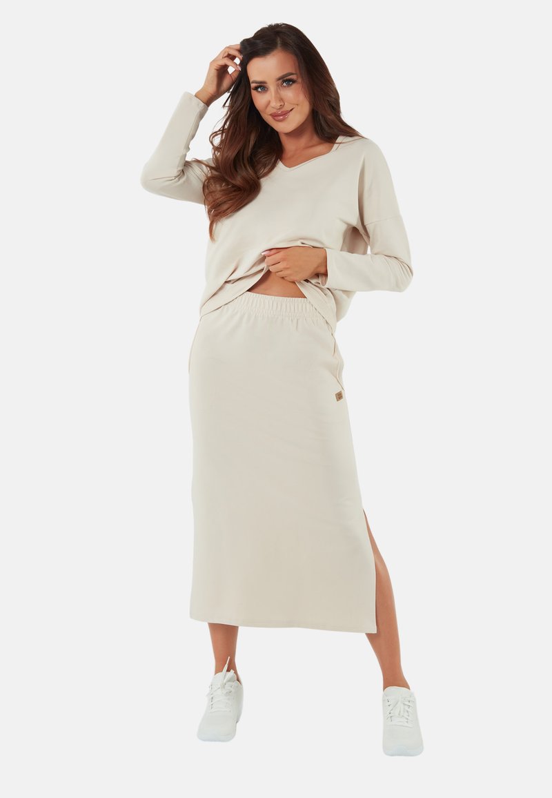Beżowa bluzka z długim rękawem i dekoltem w serek, o luźnym kroju, zestawiona z pasującą spódnicą o wysokim stanie z bocznym rozcięciem, wyróżniającą się subtelnym logo.