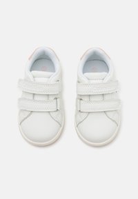 Białe sneakersy dla niemowląt wykonane z materiału syntetycznego, z podwójnymi rzepami, okrągłym noskiem oraz miękkim, wyściełanym kołnierzem kostki z różowymi akcentami.