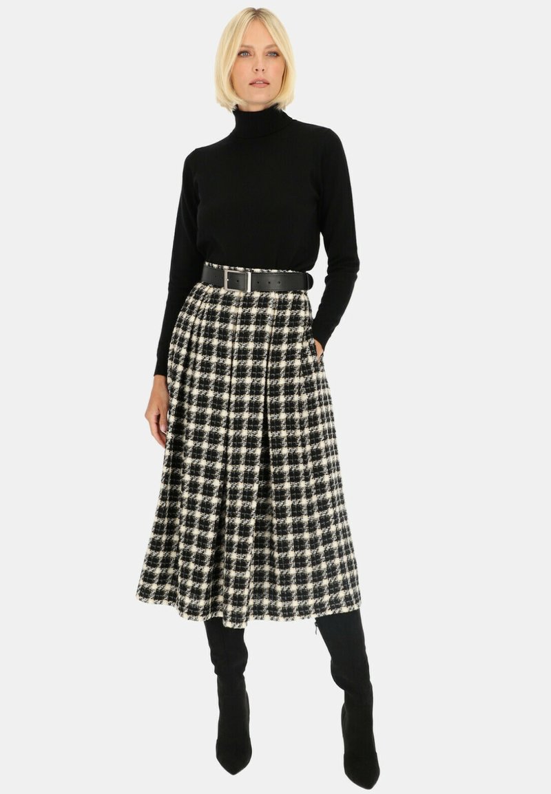Długi czarny sweter z golfem noszony z spódnicą w kratę do kolan w czerni i bieli, z pliskami i czarnym paskiem. Czarne kozaki za kolano.