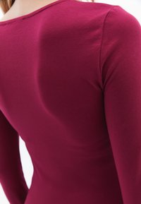 Pitkähihaista istuva paita syvässä burgundin värissä, valmistettu pehmeästä puuvillasekoitteesta. Ominaisuuksiin kuuluu pyöreä kaula-aukko ja sileä kangas, jossa on minimaalisesti saumoja.