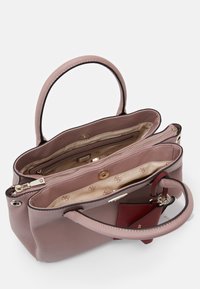 Różowa skórzana torebka z dwoma uchwytami, zamykanymi na zamek przegródkami oraz wymienną czerwoną zawieszką. Wnętrze wyłożone beżową podszewką z wzorem logo.