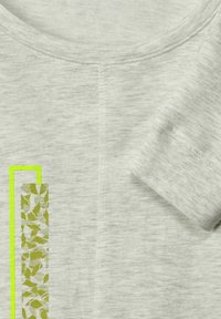 Camiseta de manga corta en gris claro con escote redondo. Presenta un patrón de hojas verdes y un contorno verde brillante a lo largo de un lado. Textura suave.