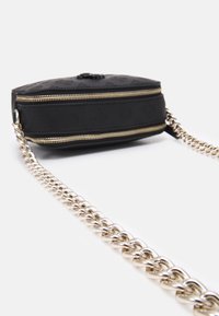 Musta tekstituurilla laukku kultaisilla vetoketjun yksityiskohdilla, jossa on ketjuolkaimet ja kohokuvioitu pinta. Kompakti suorakulmainen muoto.