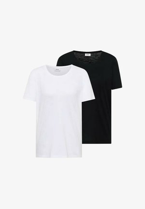 Jeune femme en t-shirt noir et jean bleu clair s'appuie contre un mur, portant un sac à bandoulière noir et des baskets blanches.