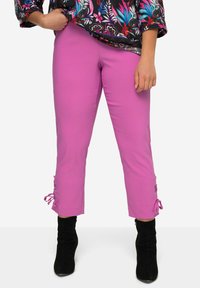 Lyserøde cropped bukser med bindebånd ved læggene, parret med sorte hæl støvler. Stof er glat og strækbart. Har en slim fit.