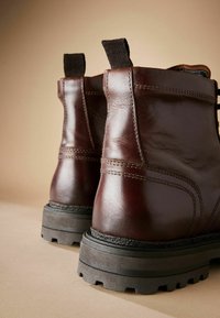 Bruine leren enkellaarzen met een gestructureerde afwerking, versterkte stiksels en een rubberen zool met diepe noppen voor grip. Inclusief elastische treklipjes.