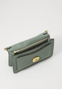 Lys grøn skinnclutch med teksturert overflate, gullfarge hardware, glidelåslukking og en frontlomme med en sirkulær trykknapp.
