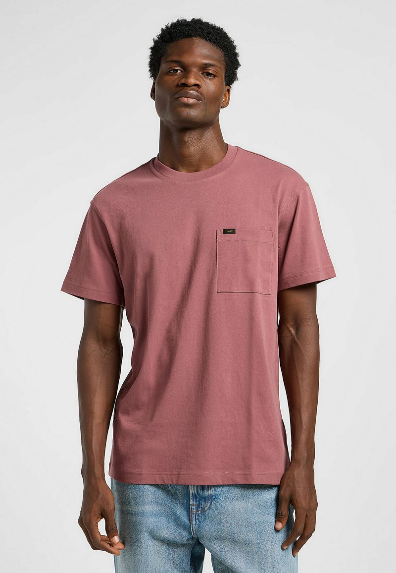 Kortärmad t-shirt med rund halsringning i dammig rosenfärgad bomull. Har en vänster bröstficka med en liten märke. Bärs med ljusblå jeans.