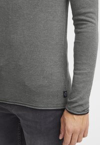 Gray long-sleeve shirt made of knit fabric with a fitted design. Features a small logo tag at the hem and contrasting cuff trim.