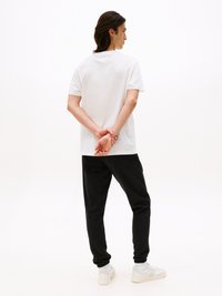 Un t-shirt en coton blanc associé à un jogging noir. Le jogging présente une taille élastique et des poignets, complété par des baskets blanches.