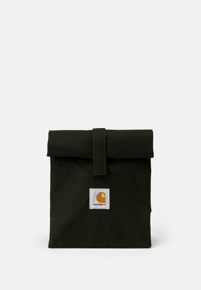 Grön canvasväska med ett vikbart lock, säkrat med ett band. Har en vit fyrkantig lapp med en orange logotyp på framsidan.