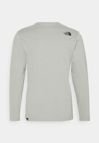 Lichtgrijze lang ingerichte T-shirt van katoen. Heeft een ronde hals en een klein zwart logo op de linkerschouder. Gladde textuur.